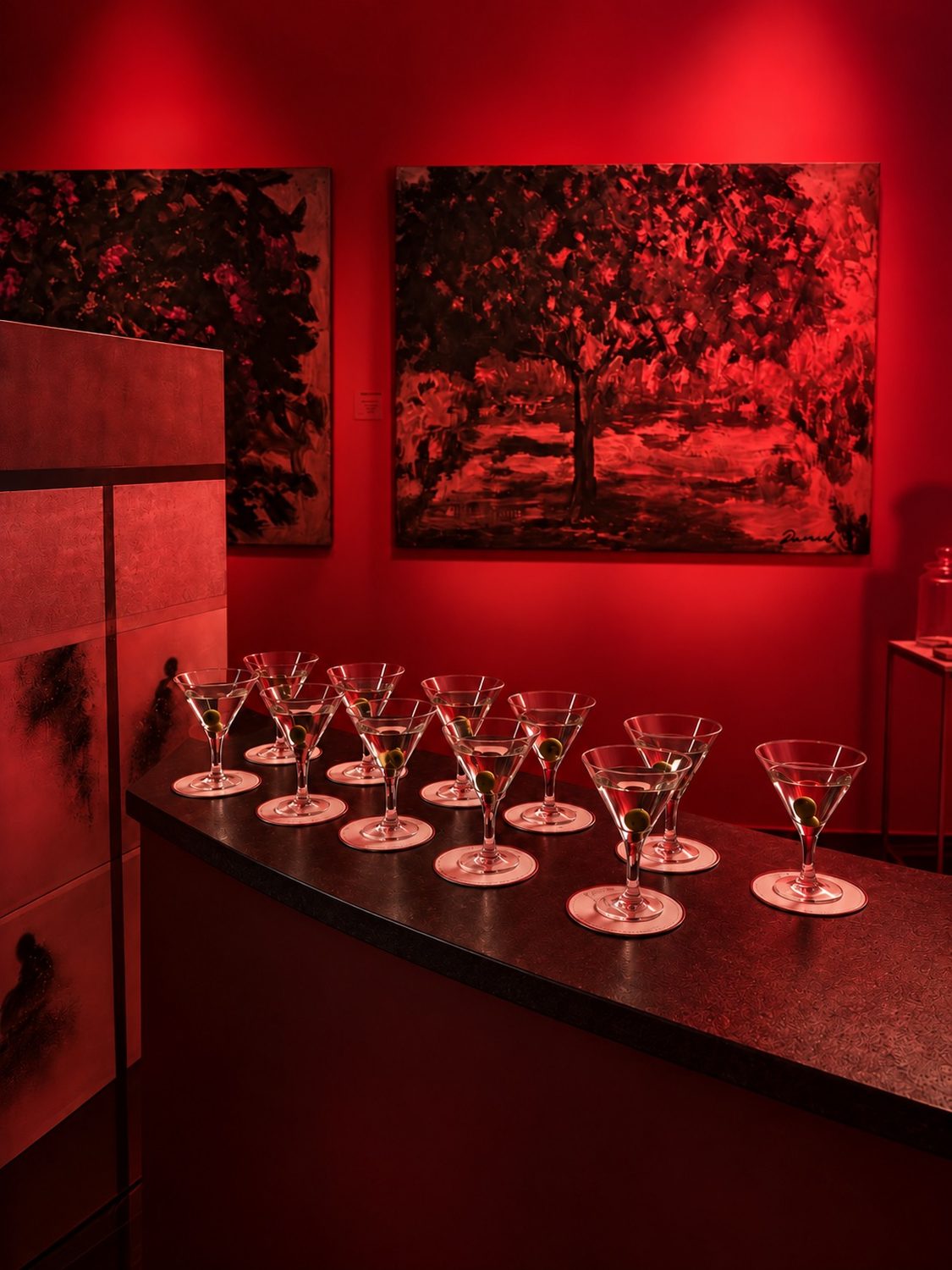 Des verres à martini alignés sur le bar de la Galerie Cheriff Tabet, Beyrouth, sous lumière rouge, des tableaux derrière